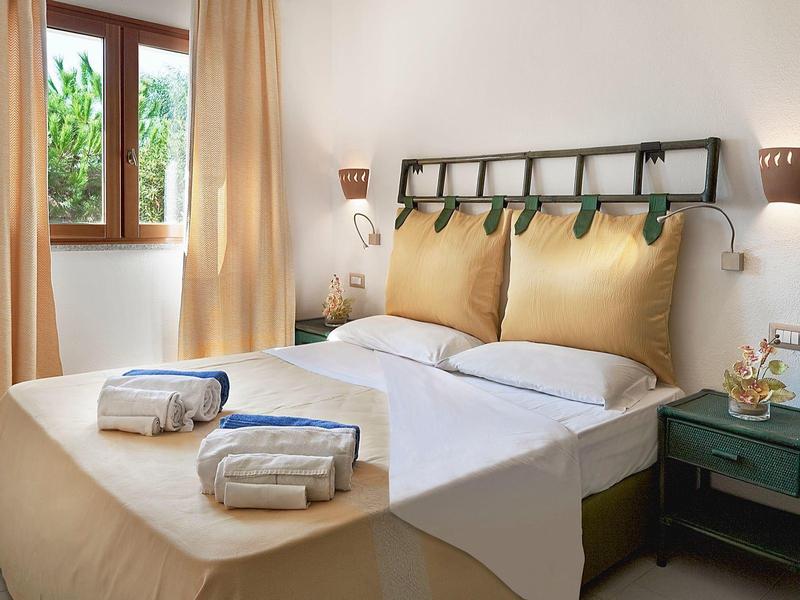 Hell eingerichtetes Schlafzimmer mit großem Bett, gepolstertem Kopfteil, zwei Handtüchern und grünem Nachttisch.