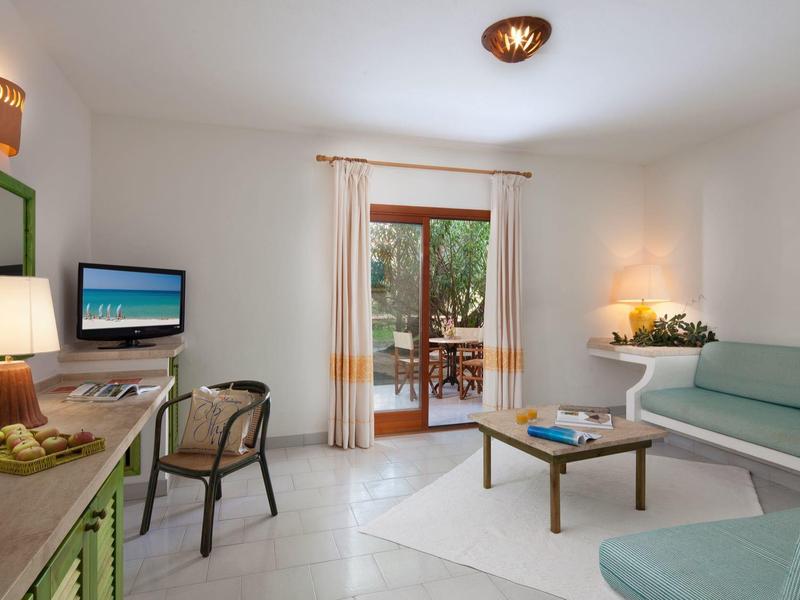 Helles Wohnzimmer mit grüner Polstersitzbank, Holztisch, Schreibtisch, TV und Zugang zu Terrasse.