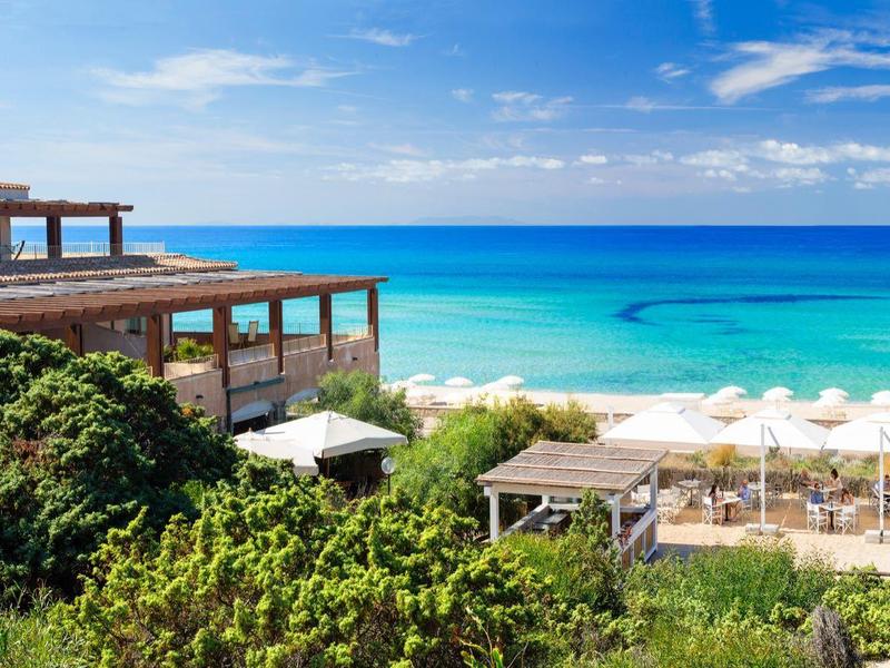 Strandresort mit Holzterrassen, grünen Pflanzen und türkisfarbenem Meer unter blauem Himmel.