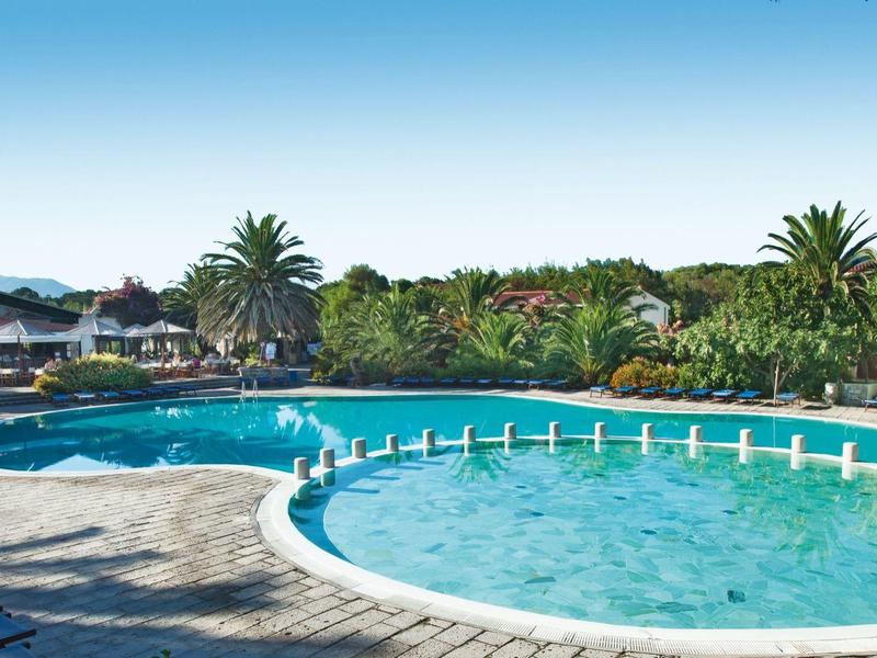 Großer Pool mit klarem Wasser, Sonnenschirmen und Liegestühlen, umgeben von Palmen und blauem Himmel.