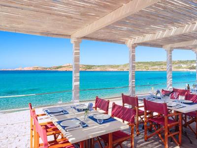 Offenes Strandrestaurant mit Holztischen und roten Stühlen unter weißem Dach mit Blick auf das blaue Meer.