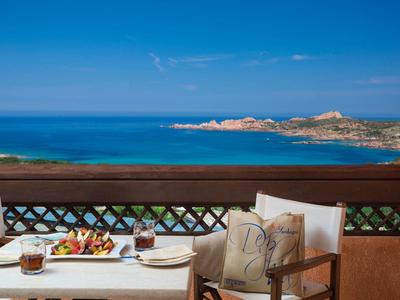 Balkon mit Tisch und Stühlen, darauf Getränke und Snacks, mit Blick auf das blaue Meer und Küste.