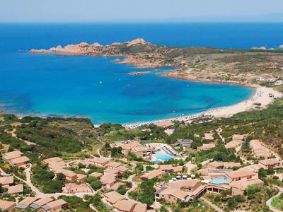 Küstenlandschaft mit türkisblauem Meer, Sandstrand und grüner Vegetation rund um Häuser.