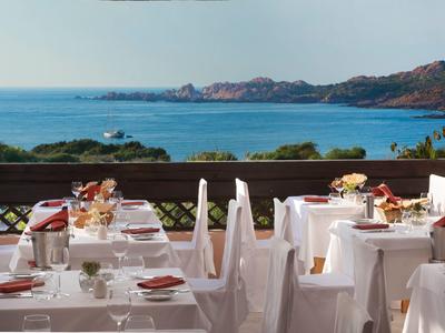 Hotel terrace with set tables overlooking the sea and coastal landscape.