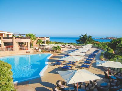 Großer Pool mit Liegen und Sonnenschirmen, Meer und blauer Himmel im Hintergrund.