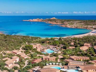 Küstenlandschaft mit blauem Meer, Sandstränden, grüner Vegetation und kleinen Häusern mit roten Dächern.