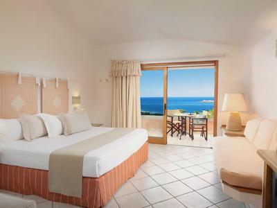 Helles Hotelzimmer mit Doppelbett, Sofa und Terrasse mit Meerblick.