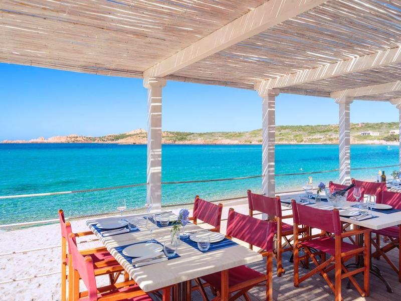 Offenes Restaurant mit Holzmöbeln am Meer und Blick auf blauen Himmel und Wasser.