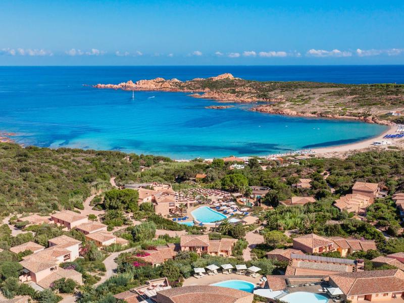Küstenlandschaft mit blauem Meer, Sandstränden, grüner Vegetation und kleinen Häusern mit roten Dächern.