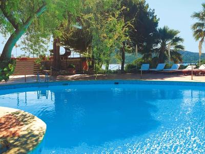 Blauer Swimmingpool mit umgebenden Bäumen und Liegestühlen unter klarem Himmel.