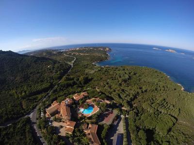 Landschaft mit dichtem Wald, Gebäuden und blauem Pool am Küstenhang unter klarem Himmel.