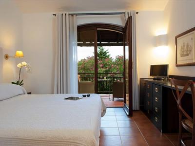 Helles Schlafzimmer mit Doppelbett, Schreibtisch, Stuhl, offenen Balkonfenstern und weißer Wanddekoration.