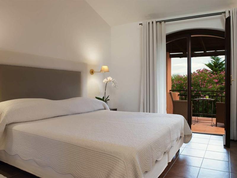 Schlichtes Schlafzimmer mit Doppelbett, grauem Kopfteil, weißer Bettwäsche und Zugang zu Balkon.