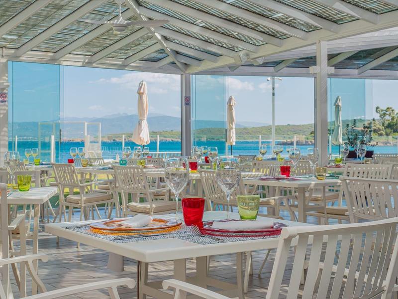 Terrasse lumineuse et ouverte d'un restaurant en bord de mer avec tables blanches et vue océan.