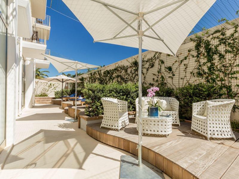 Terrasse moderne avec des chaises blanches, un sol en bois et de grands parasols sous un ciel clair.