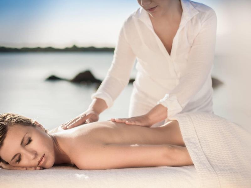 Femme recevant un massage relaxant en plein air avec une mer calme en arrière-plan.