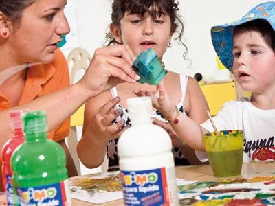 Drei Personen sitzen am Tisch und führen ein Bastelprojekt mit Farben und Pinseln durch.