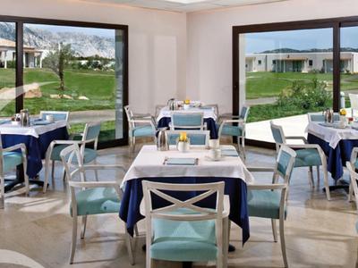 Helles Restaurant mit großen Fenstern, blauen und weißen Stühlen und weiß gedeckten Tischen.