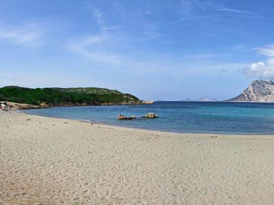 Weitläufiger Sandstrand mit ruhigem blauem Wasser und grün bewaldeten Inseln im Hintergrund.