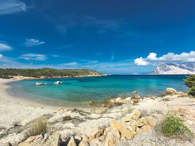 Strand mit weißem Sand, klarem türkisfarbenem Wasser und bewölktem Himmel.