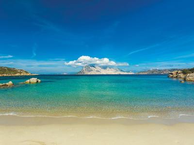 Klares türkisfarbenes Meer mit Sandstrand und blauem Himmel mit Wolken.