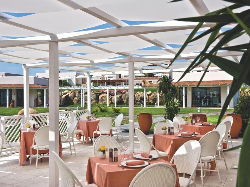 Freiluft-Restaurant mit orangefarbenen Tischdecken und weißen Stühlen unter einer Pergola.