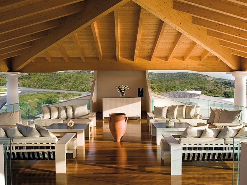 Offener Lounge-Bereich mit Holzboden, weißen Sofas, Kamin und Blick auf Wasser und Hügel.