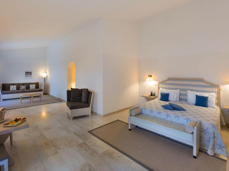 Helles Hotelzimmer mit großem Bett, Sessel, Schreibtisch und minimalistischer Einrichtung.