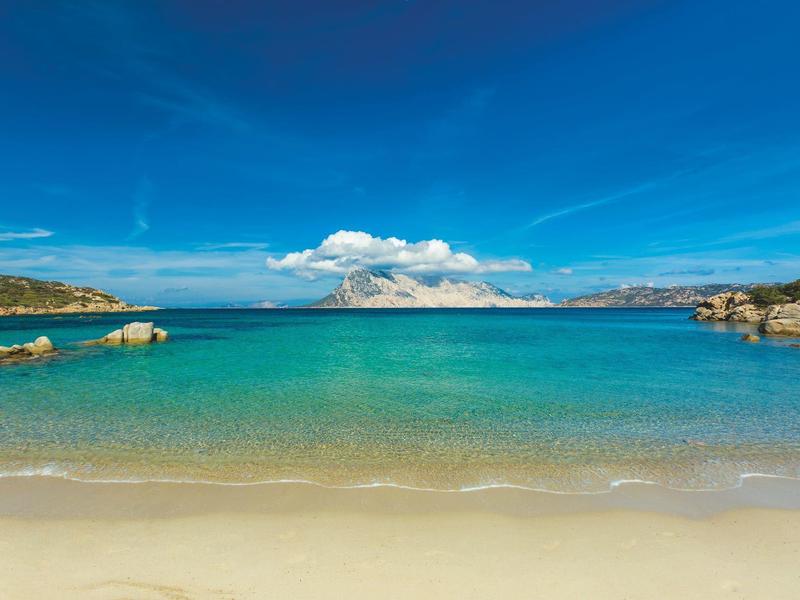 Klares türkisfarbenes Meer mit Sandstrand und blauem Himmel mit Wolken.