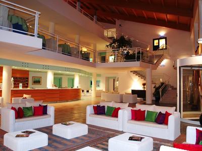 Espace lounge d'hôtel moderne avec canapés blancs, coussins colorés et sol en bois.