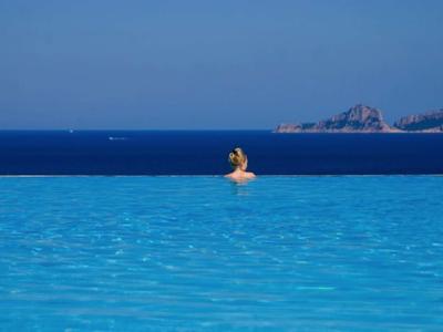 Personne nage dans une piscine à débordement avec vue sur la mer bleue et la côte.