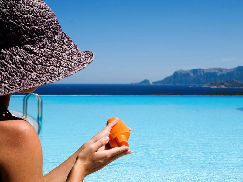 Personne avec chapeau de soleil admire l'eau turquoise et montagnes lointaines.