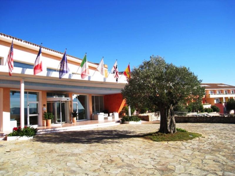 Bâtiment d'hôtel avec drapeaux et un grand arbre sur une aire pavée sous un ciel dégagé.