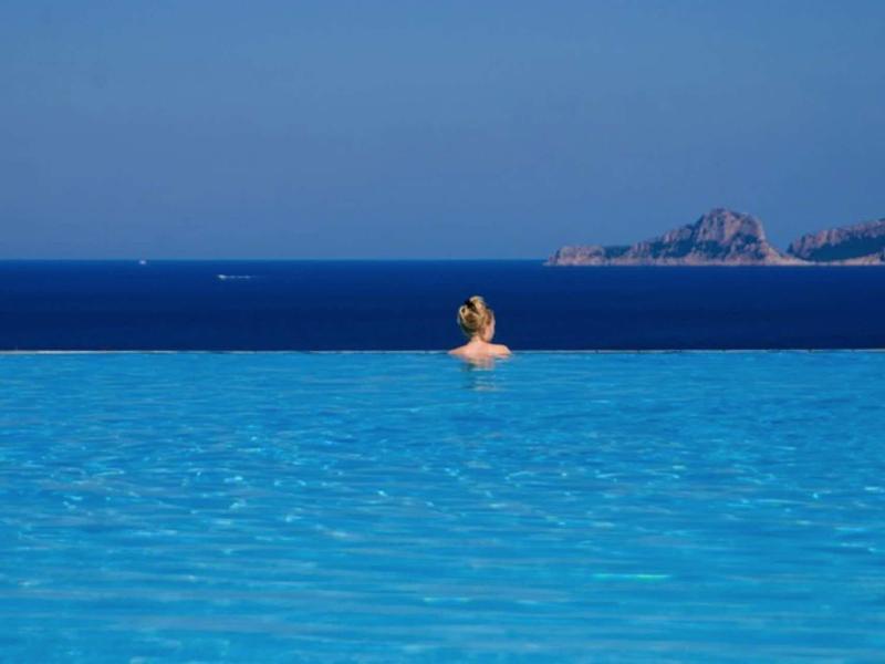 Personne nage dans une piscine à débordement avec vue sur la mer bleue et la côte.