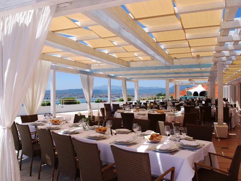 Terrasse couverte avec tables dressées offrant une vue sur la mer dans un hôtel.
