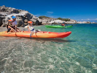 Two people sit in a double kayak on clear water near rocky shore.
