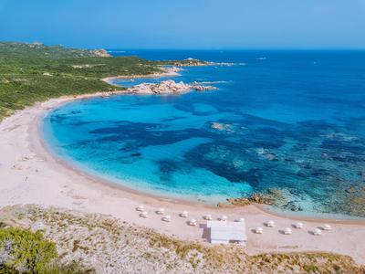 Langer Strand mit klarem, türkisblauem Wasser, umgeben von grüner Vegetation und felsiger Küste.