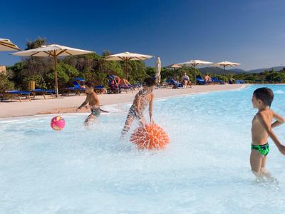 Bambini che giocano con palle d'acqua nella zona bassa di una piscina all'aperto con tempo soleggiato.