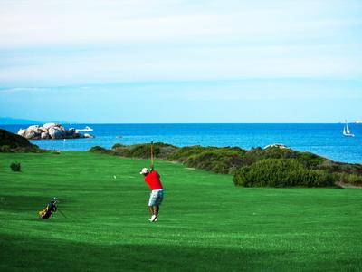 Golfer in red shirt playing on green coastal golf course with sea view.