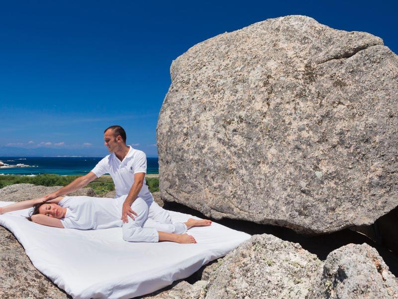 Massaggio all'aperto su un materasso morbido tra grandi rocce sotto un cielo azzurro brillante.