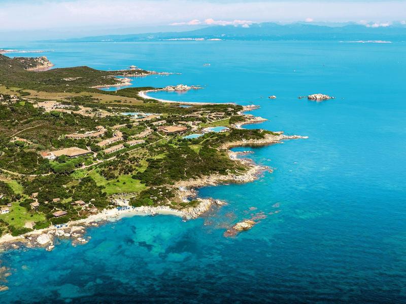 Veduta aerea di una costa rocciosa con vegetazione verde e acqua azzurra limpida.