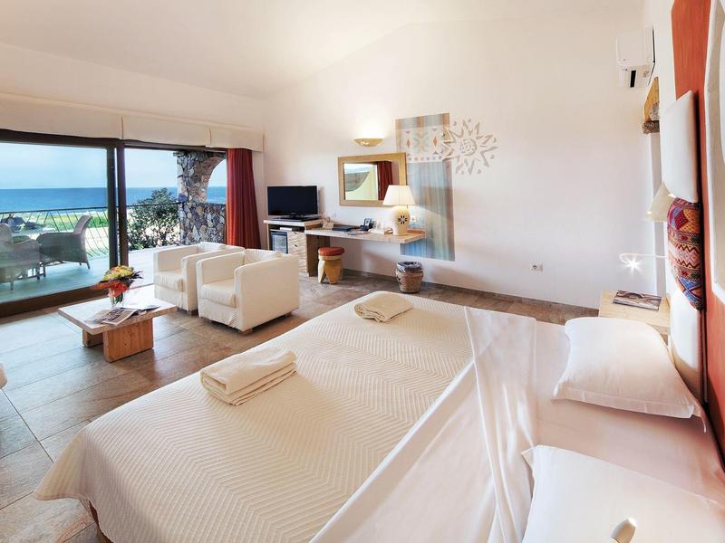 Camera d'hotel luminosa con letto matrimoniale, divano e vista sul mare attraverso ampie finestre.