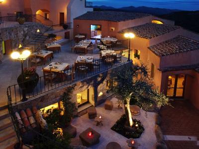 Vista serale di un ristorante su terrazza con tavoli illuminati e vista sulle colline sotto un cielo blu.