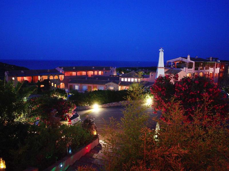 Scatto notturno di un hotel illuminato con giardino e sentiero in primo piano.