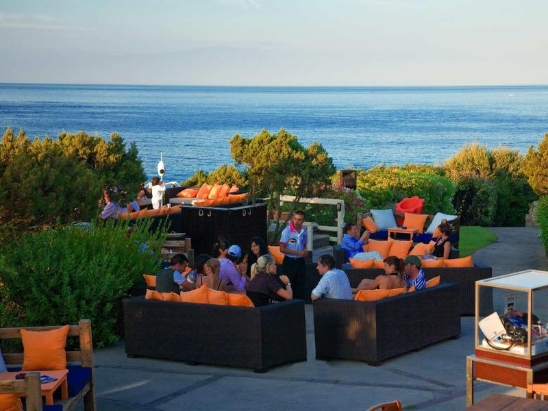 Persone si rilassano su una terrazza all'aperto con vista sul mare in una giornata di sole.