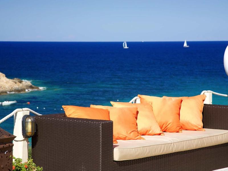 Area esterna moderna con divano e cuscini arancioni vista mare blu e barche a vela.