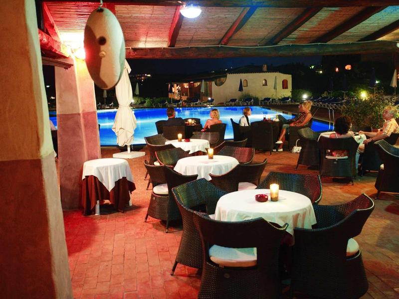 Accogliente terrazza esterna con tavoli rotondi e sedie vicino a piscina illuminata di notte.