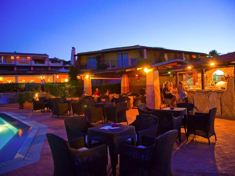 Accogliente area esterna dell'hotel con piscina e tavoli apparecchiati al crepuscolo.