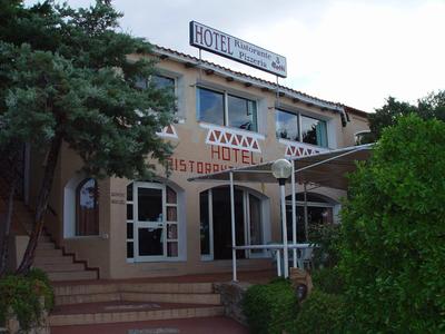 Eingang eines zweistöckigen Hotels mit Treppen, Bäumen und grünem Busch im Vordergrund.