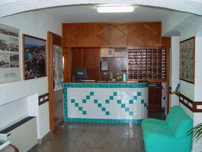 Hell beleuchteter Empfangsbereich mit türkis-weiß gekacheltem Tresen und grünem Sofa rechts.